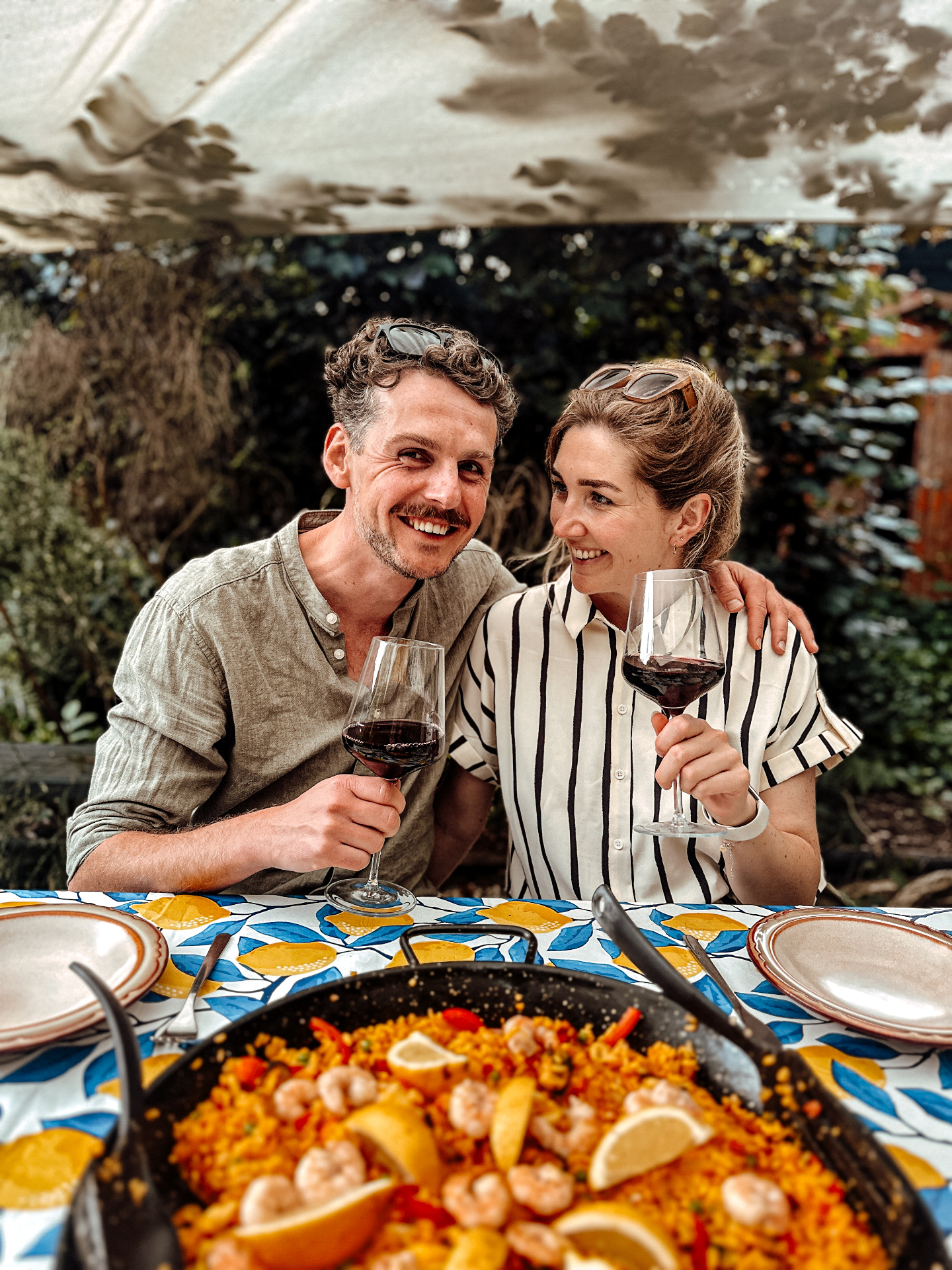Anne and Freek raising glasses of red wine over a paella