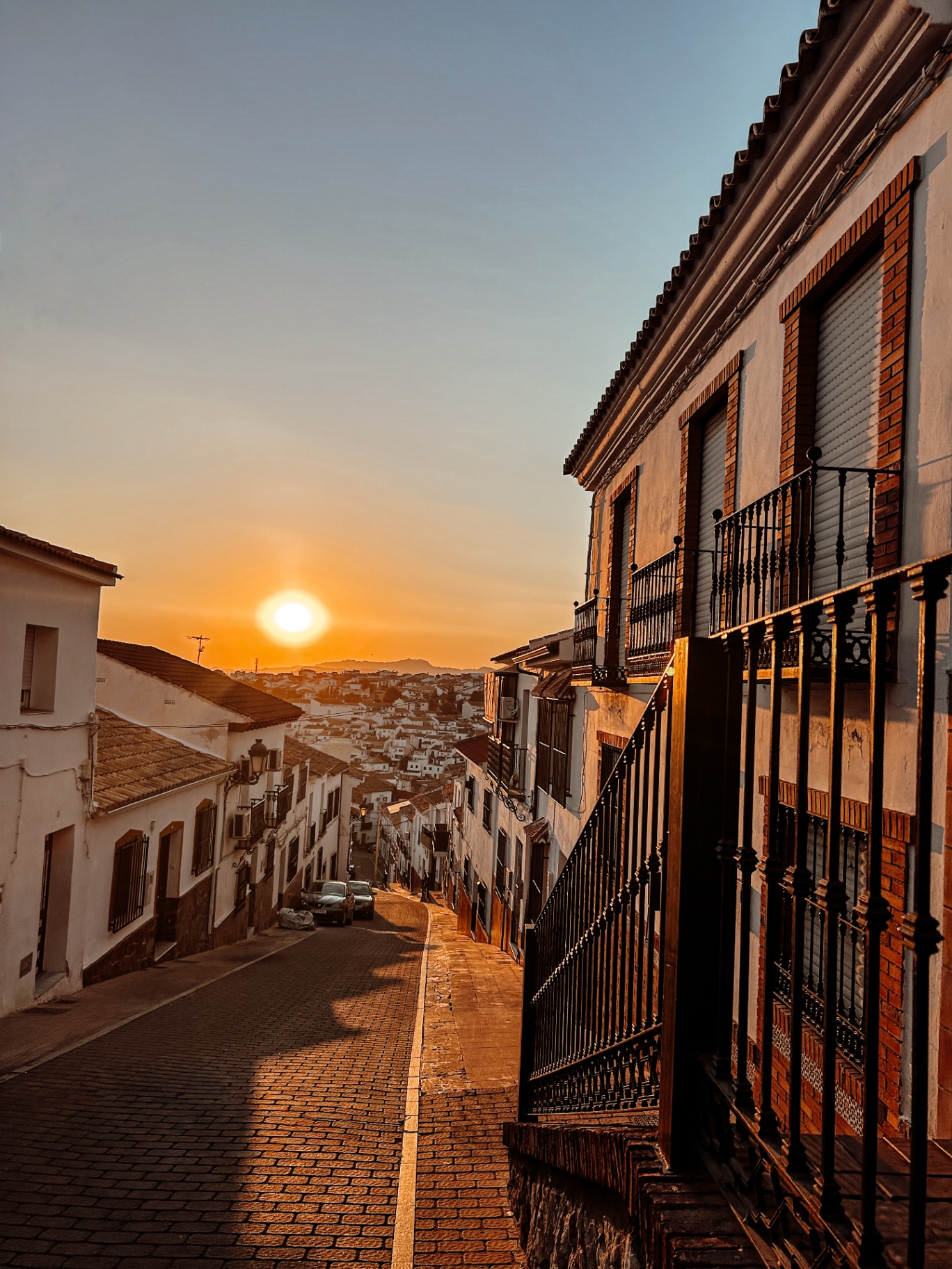 Sunset over a cobbled street in Colmenar, with whitewashed houses and balconies